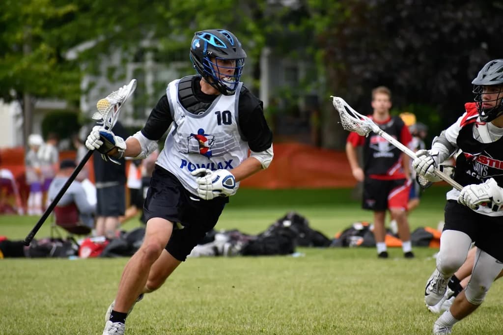 POWLAX midfielder in a white jersey running upfield with the ball during a game as a defender pursues